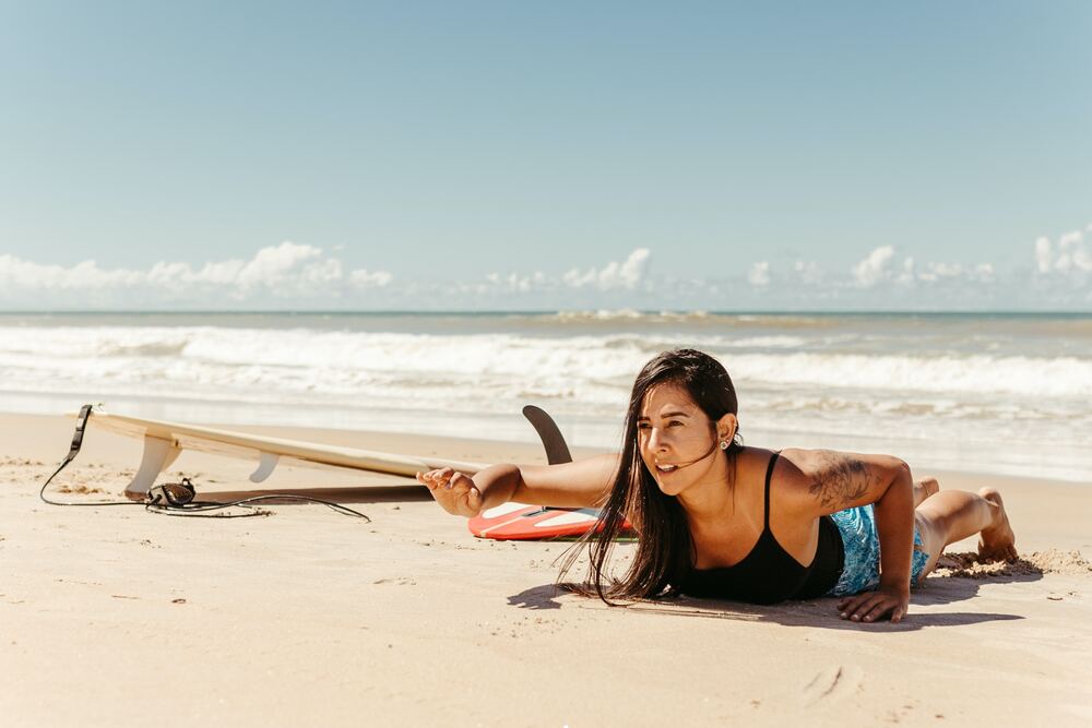 Chica practicando la puesta en pie de surf en arena para evitar errores más comunes de aprender a hacer surf